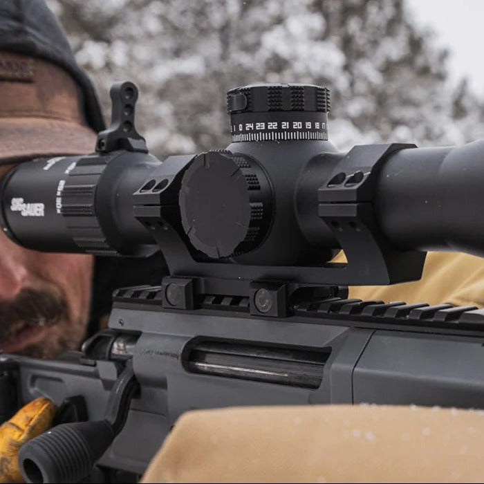 Person aiming a rifle with a scope in a forest setting