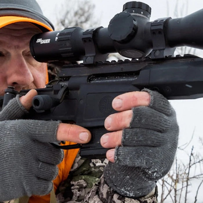 Person in camouflage holding a rifle with a scope in a snowy forest setting